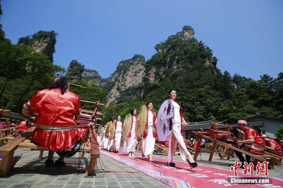 6月7日，第十三個中國“文化和自然遺產(chǎn)日”即將來臨之際，近百名土家織錦工人走進世界自然遺產(chǎn)地湖南張家界武陵源，在山水峰林間向中外游客展示國家級非物質文化遺產(chǎn)土家織錦技藝。當?shù)仄炫蹛酆谜哌€現(xiàn)場走秀，展示土家織錦提包、圍巾等旅游產(chǎn)品。中新社發(fā) 吳勇兵 攝